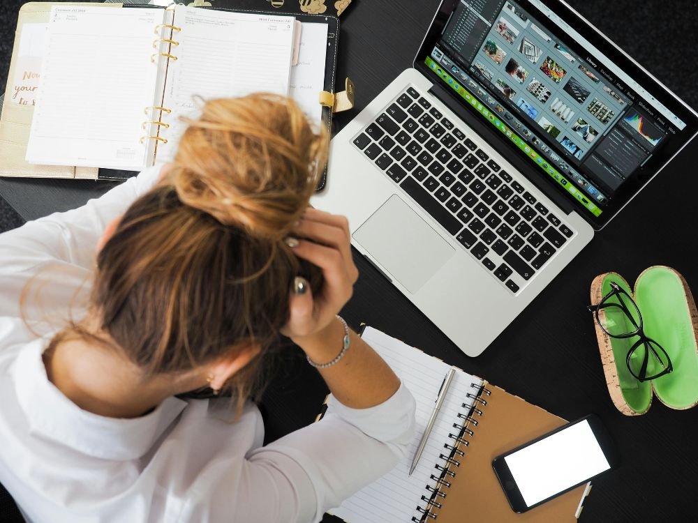 Mulher sentada em frente ao computador com muitas coisas para fazer e estressada. um pessoa que precisa aplicar as dicas do artigo sobre como reduzir o stress