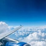 Vista aérea de um avião em pleno voo acima das nuvens, com céu azul claro e uma turbina em destaque. A imagem transmite a sensação de viagem e liberdade, simbolizando o universo das milhas aéreas — tema central do artigo: 5 Erros Comuns ao Usar Milhas – E Como Evitá-los