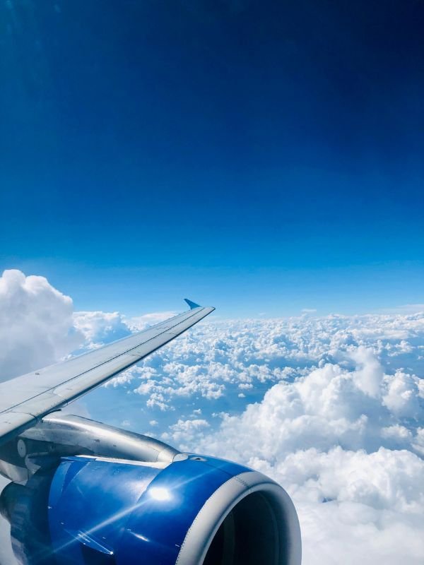 Vista aérea de um avião em pleno voo acima das nuvens, com céu azul claro e uma turbina em destaque. A imagem transmite a sensação de viagem e liberdade, simbolizando o universo das milhas aéreas — tema central do artigo: 5 Erros Comuns ao Usar Milhas – E Como Evitá-los