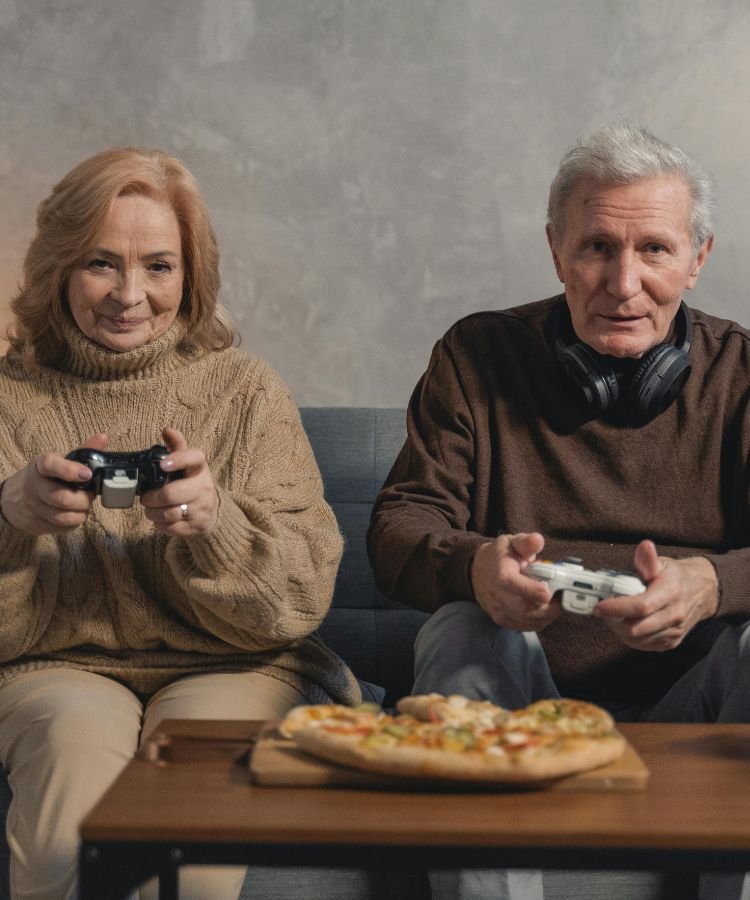 "Coisas que fazemos hoje que nossos avós achariam estranhas" – Na imagem, um casal de idosos se diverte jogando videogame lado a lado, com fones de ouvido e uma pizza sobre a mesa. Uma cena moderna e descontraída que ilustra com bom humor como os hábitos das novas gerações podem parecer curiosos – e até impensáveis – para os mais antigos.