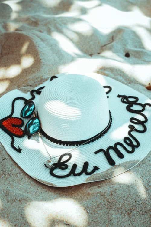 Chapéu de praia com a seguinte frase: Eu mereço, na areia da praia. para ilustrar como essa ideai do eu mereço te sabota Às vezes
